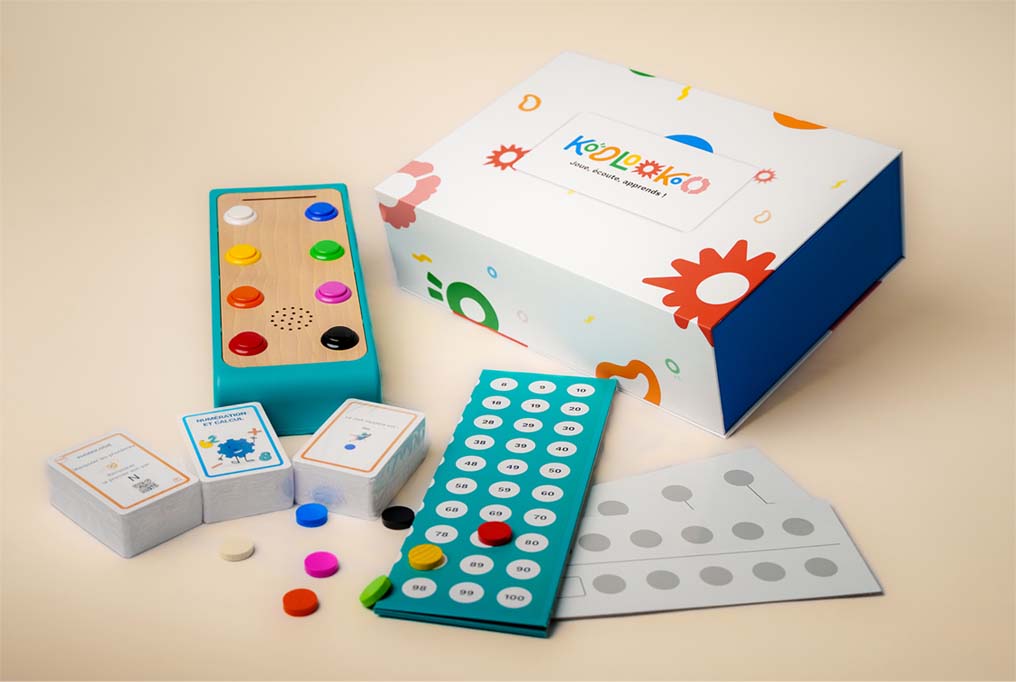 Photographie de l'ensemble Koolookoo, Boite station de jeu, cartes, jetons, planches de réponse et plateau de jeu.