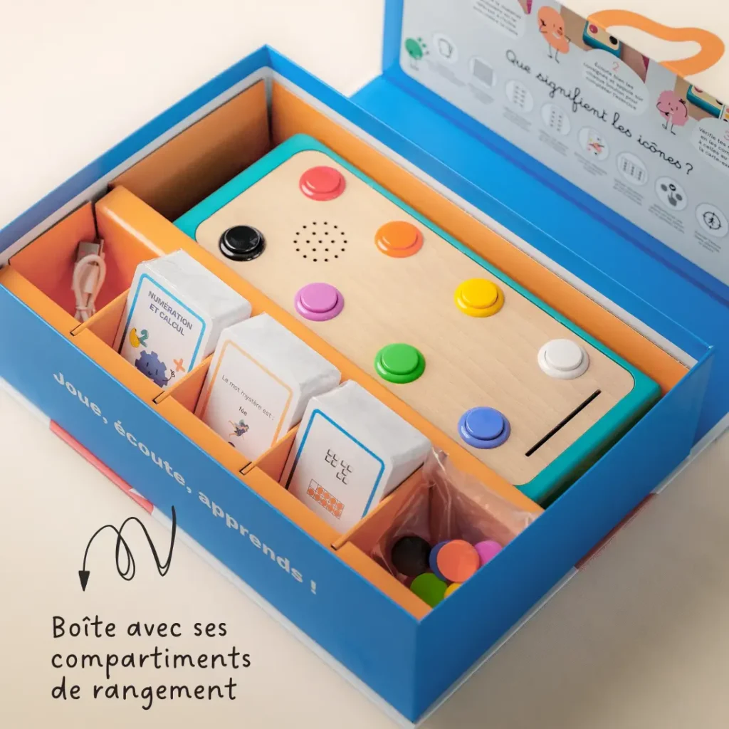 Boîte de rangement ouverte contenant le jeu éducatif avec cartes pédagogiques, pions colorés et station à boutons.