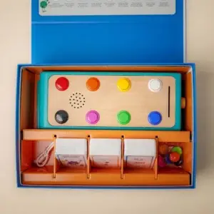 Boîte du jeu Koolookoo ouverte montrant la station éducative, les cartes d’activités et les pions colorés.