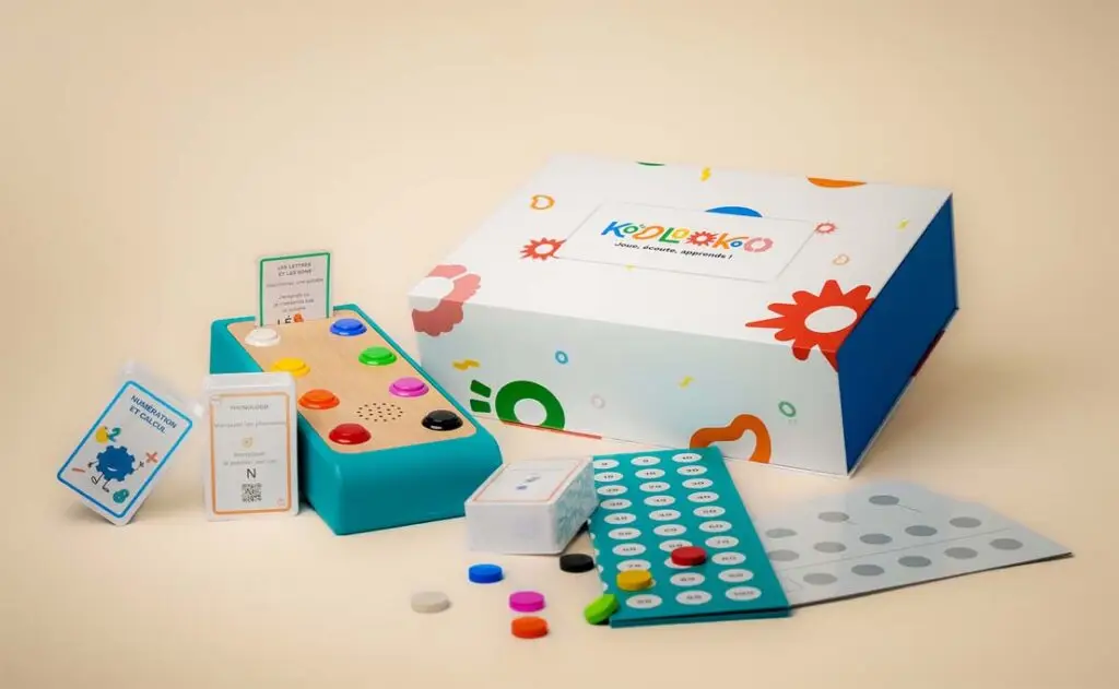 Photographie de l'ensemble Koolookoo, Boite station de jeu, cartes, jetons, planches de réponse et plateau de jeu.